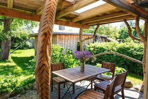 A wooden pergola with a table and chairs underneath, surrounded by greenery. - Grethe Ground Floor || Rockow (Rockow)