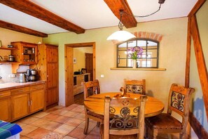 A wooden kitchen with a round dining table and chairs, a hanging light fixture, and a window with a flower vase. - Grethe Ground Floor || Rockow (Rockow)