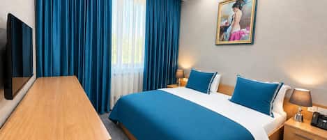 A hotel room with a bed, a desk, a TV, and a painting on the wall.