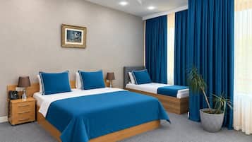 A hotel room with two beds, a nightstand, a lamp, a framed picture on the wall, and a potted plant.