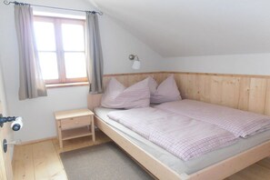 A single bed with a headboard, a bedside table, a lamp, and a window with curtains. - Gaiswinkler holiday home (Grundlsee)