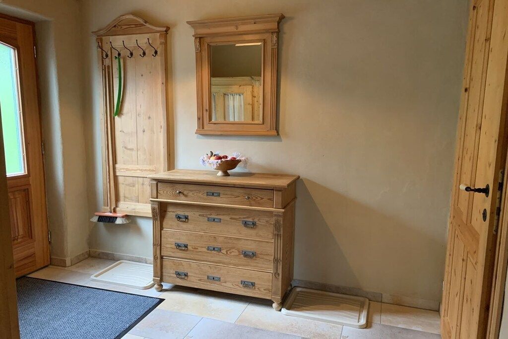 A wooden dresser with multiple drawers and a mirror above it, positioned in a room with a door and a window.