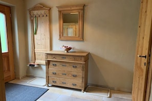 Une commode en bois, dotée de nombreux tiroirs et surmontée d’un miroir, est placée dans une pièce qui possède une porte et une fenêtre.