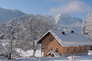 Un chalet en bois, doté d’un toit en pente, entouré d’arbres couverts de neige et avec des montagnes en arrière-plan.