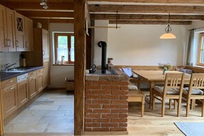 A kitchen with wooden cabinets, a brick island, a dining table with chairs, and a hanging light fixture. - Gaiswinkler holiday home (Grundlsee)