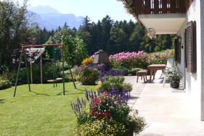 A garden with a swing set, potted plants, and a patio area with a table and chairs. - Holiday apartment with 2 bedrooms (Hofstetten)