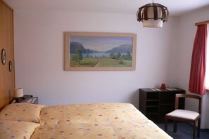 A hotel room with a bed, a desk, a chair, a painting on the wall, and a hanging light fixture. - Holiday apartment with 2 bedrooms (Hofstetten)