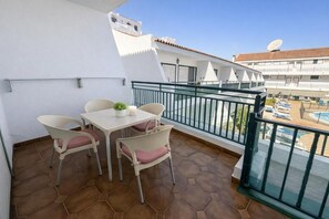 A balcony with a table and chairs, a potted plant, and a view of a swimming pool and buildings. - Apartment Chipeque (Arona)