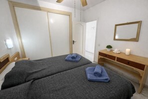 A hotel room with two beds, a wooden dresser, a mirror, and a door leading to another room. - Apartment Chipeque (Arona)