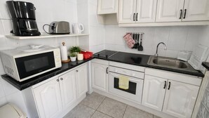 Uma cozinha com armários brancos, bancada preta, micro-ondas, cafeteira, torradeira e pia.