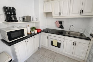 A kitchen with white cabinets, a black countertop, a microwave, a coffee maker, a toaster, and a sink. - Apartment Chipeque (Arona)