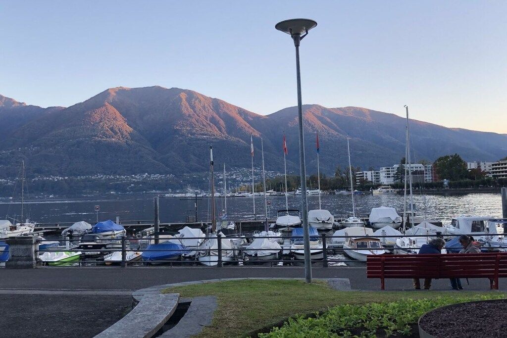 Ein Yachthafen mit vertäuten Booten, einer Bank und Bergen im Hintergrund.