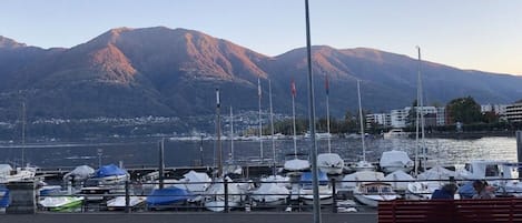 Ein Yachthafen mit vertäuten Booten, einer Bank und Bergen im Hintergrund.