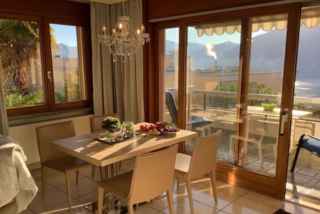 A dining area with a table set for two, a chandelier, and a view of the ocean through large sliding glass doors.