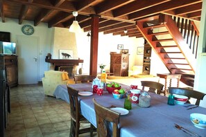 A dining area with a table set for four, surrounded by wooden chairs. A fireplace is visible in the background, and a staircase leads to an upper level. - Lovely Holiday Home in Sarzeau for 8 (Sarzeau)