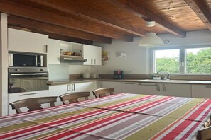 A kitchen with modern appliances, a dining table with chairs, and a window with a view of greenery. - Lovely Holiday Home in Sarzeau for 8 (Sarzeau)
