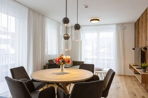 A modern dining area with a round wooden table, black chairs, and a vase of flowers. - OFS_C_FW_2SZ_m.T._mH_FIS_13 (Fiss)