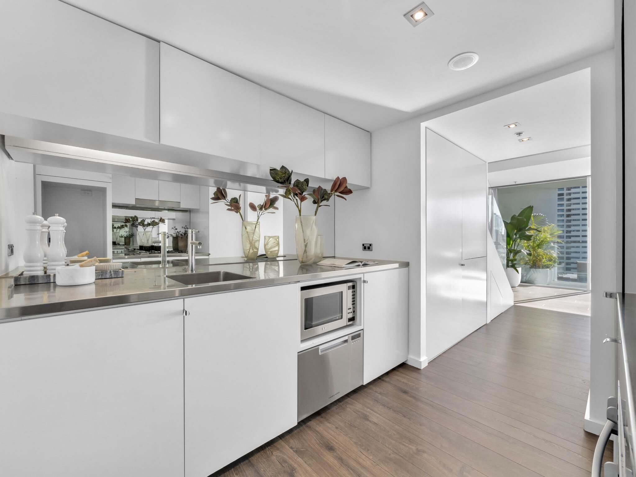 A modern kitchen with white cabinetry, a stainless steel countertop, a built-in oven, and a large window offering a view of the city.