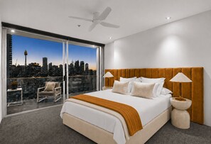 Ein modernes Schlafzimmer mit Blick auf die Stadt, einem großen Bett, zwei Nachttischlampen und einem Deckenventilator.