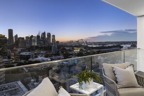 Ein hoher Balkon mit Blick auf die Stadt, einer Glastrennwand und einem kleinen Tisch mit einer Pflanze.