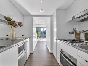 A modern kitchen with stainless steel appliances, a wooden floor, and a view to the outside. - Harbour Muse - Stylish 2 or 3 Bedroom Apartment with Spectacular Harbour Views (Darlinghurst)
