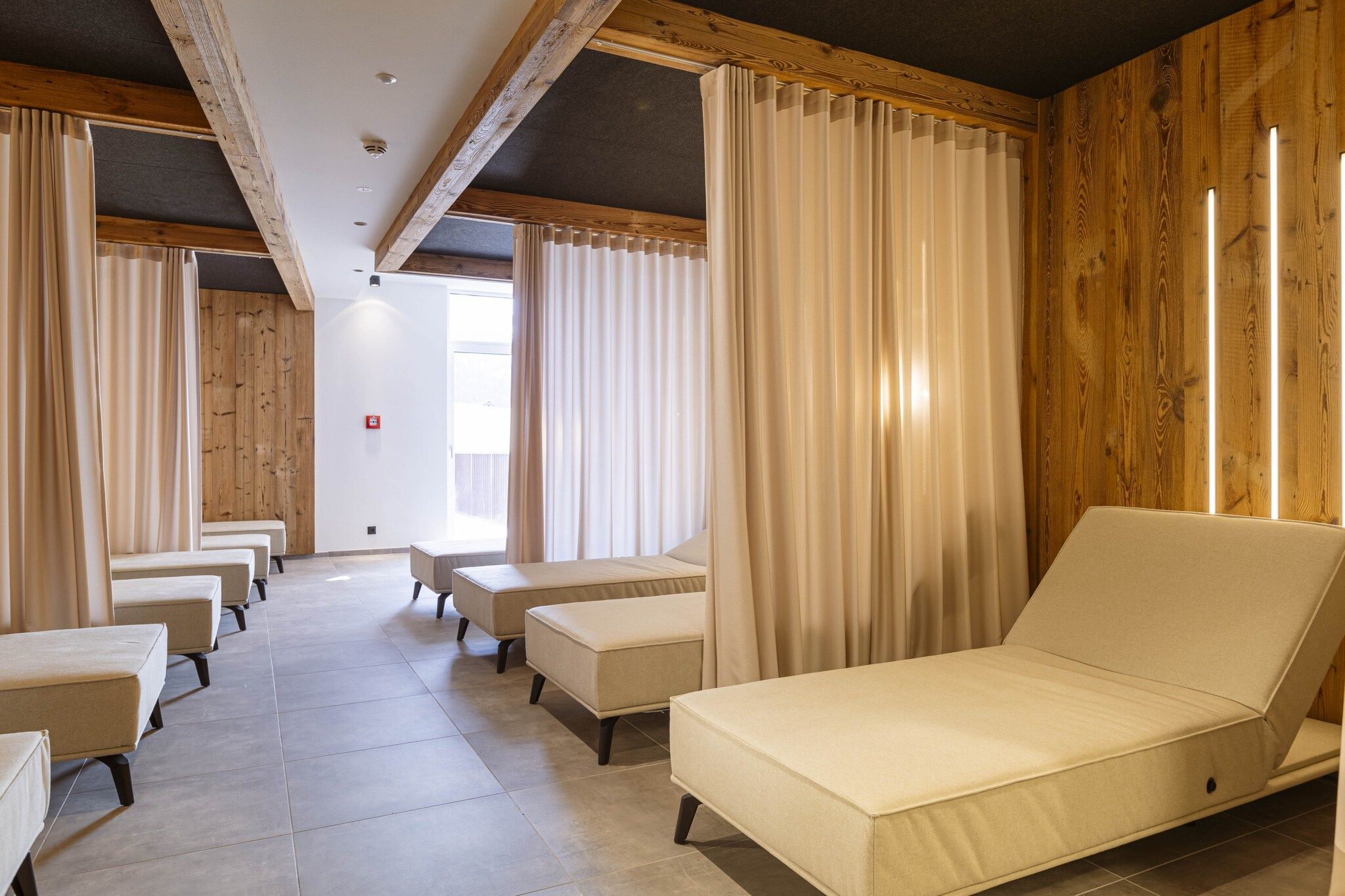 A room with a bed, two chairs, and a bench. There are curtains on the windows.