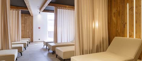 A room with a bed, two chairs, and a bench. There are curtains on the windows.