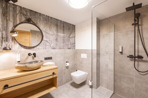 Un baño moderno con lavabo de piedra, inodoro y cabina de ducha con mampara de vidrio.