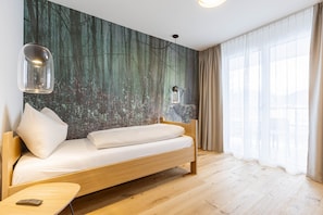 Un dormitorio moderno con una cama de madera, un mural en la pared, una lámpara colgante y un ventanal con cortinas traslúcidas.