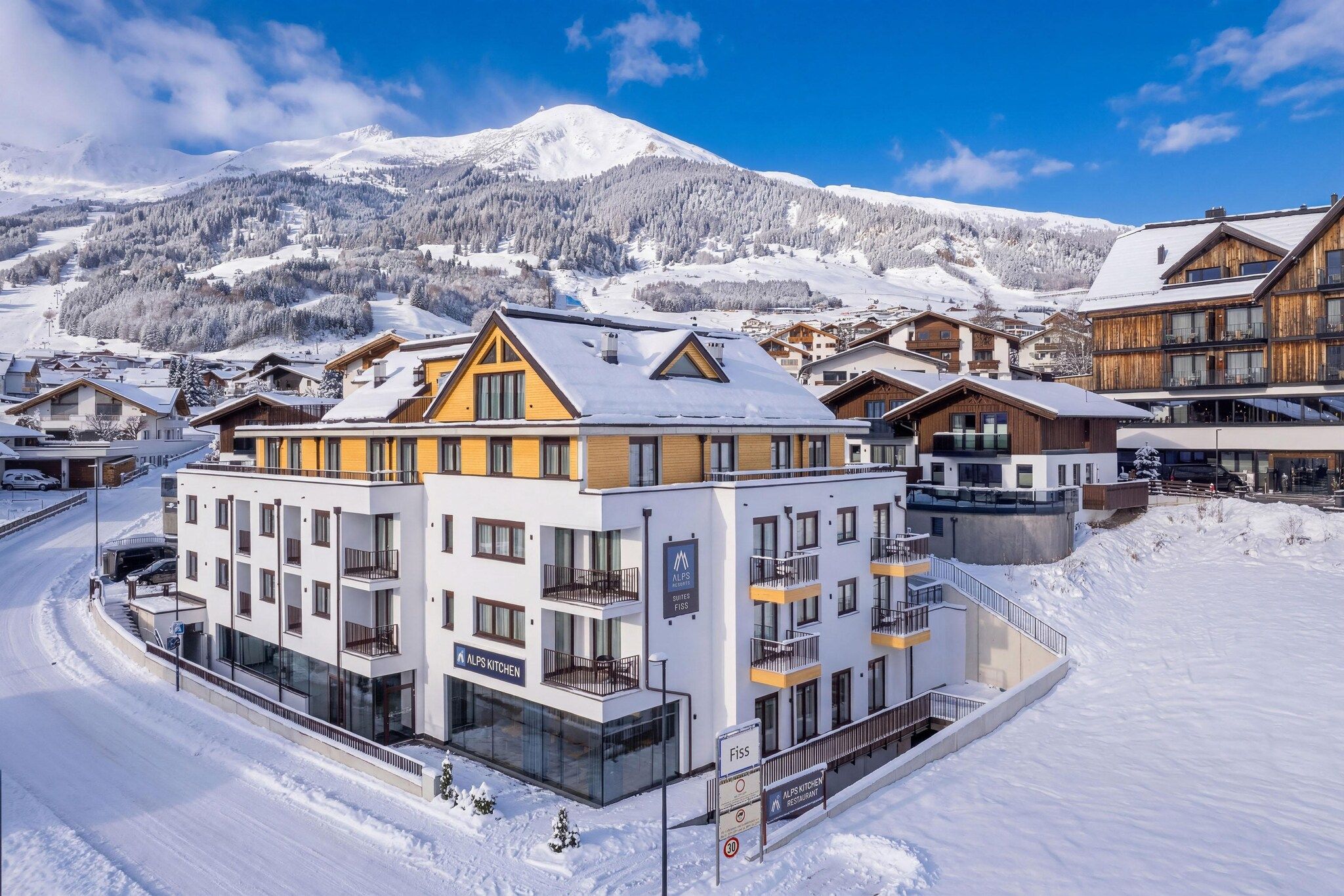 A hotel with multiple floors, balconies, and a sign indicating it is part of the Alps Resorts.