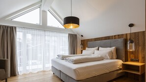 Et moderne soveværelse med en stor seng, et træhovedgærde, en hængende lampe og udsigt gennem lette gardiner.