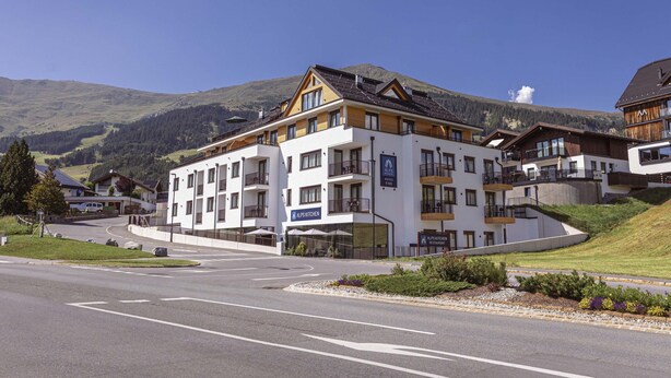 Et hotel med flere etager, en restaurant og et køkken, omgivet af et bjergrigt landskab.