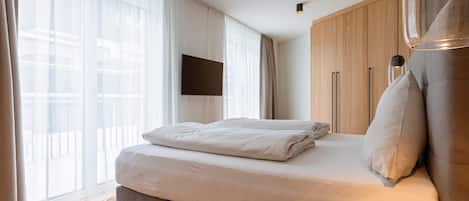A modern hotel room with a large bed, a flat-screen TV mounted on the wall, and a wooden wardrobe.