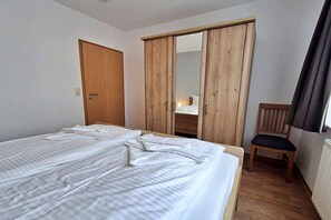 A bedroom with two beds, a wooden wardrobe, a chair, and a window with curtains.
