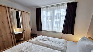 Une chambre d’hôtel avec deux lits, une armoire en bois, une fenêtre avec des rideaux et un radiateur.