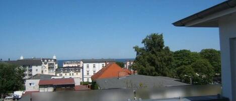 A residential building with a flat roof, a balcony, and a view of other buildings and trees.