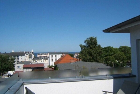 A residential building with a flat roof, a balcony, and a view of other buildings and trees.