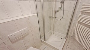 Une douche avec une porte en verre, un mur recouvert de carreaux blancs et un radiateur blanc.