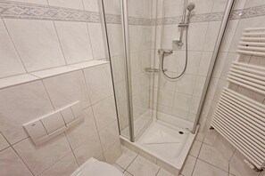 En dusch med en glasdörr, en vit kakelbeklädd vägg och ett vitt element.