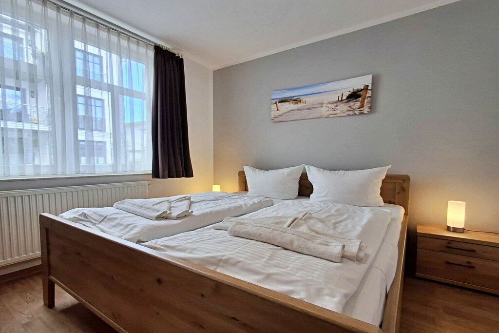 Ein Hotelzimmer mit einem hölzernen Bett, zwei Nachttischen, einem fenster mit Vorhängen und einem Wandbild.