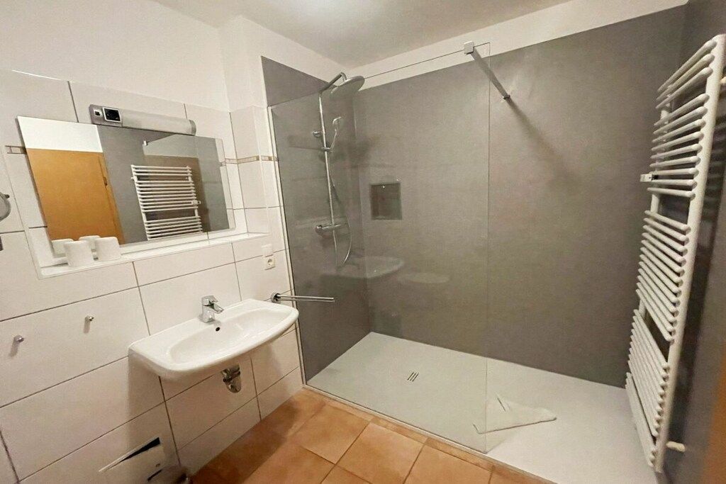 A modern bathroom with a glass-enclosed shower, a white sink, and a towel rack.