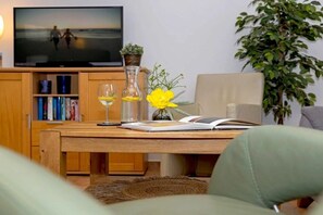 A living room with a television, bookshelves, a wooden table, and a plant. - Apartment building Linquenda 08 (Ahlbeck (Seebad))