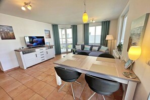 Ein modernes Wohnzimmer mit einer Couch, einem Esstisch mit Stühlen, einem Fernseher und einer Küchenzeile.