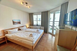Ein Hotelzimmer mit einem Doppelbett, einem Schreibtisch, einem Fernseher und einem großen Fenster mit Vorhängen.