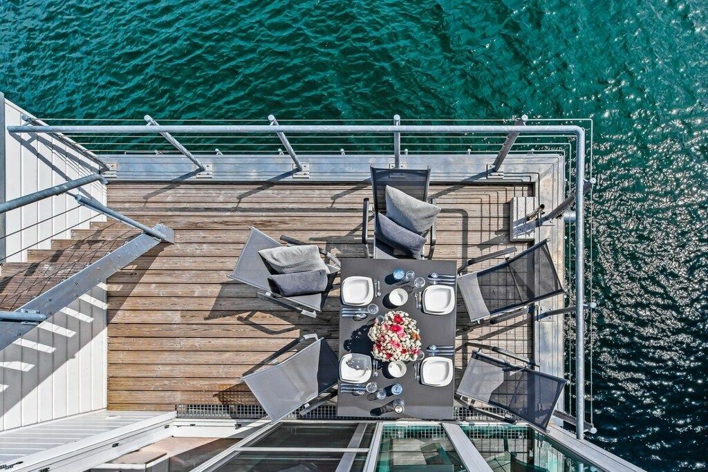 Een terras met een tafel voor vier personen, omringd door stoelen, op een houten terras met uitzicht op de oceaan.