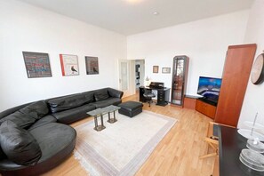 A modern living room with a black leather sofa, a glass coffee table, and a flat-screen TV. There are framed pictures on the wall and a wooden cabinet with a mirror. - Holiday apartment Bülowstraße (Heringsdorf (Seebad))