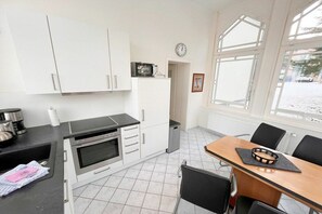 A compact kitchen with white cabinets, a microwave, and a dining area with a table and chairs. - Holiday apartment Bülowstraße (Heringsdorf (Seebad))