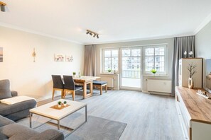 A modern living room with a sofa, a coffee table, and a dining area with chairs and a table. - Holiday apartment with 1 bedroom (Ahlbeck (Seebad))