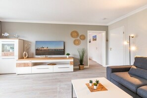 Een moderne woonkamer met een flatscreen televisie, een bank, een bijzettafeltje met planten en een minimalistisch design.