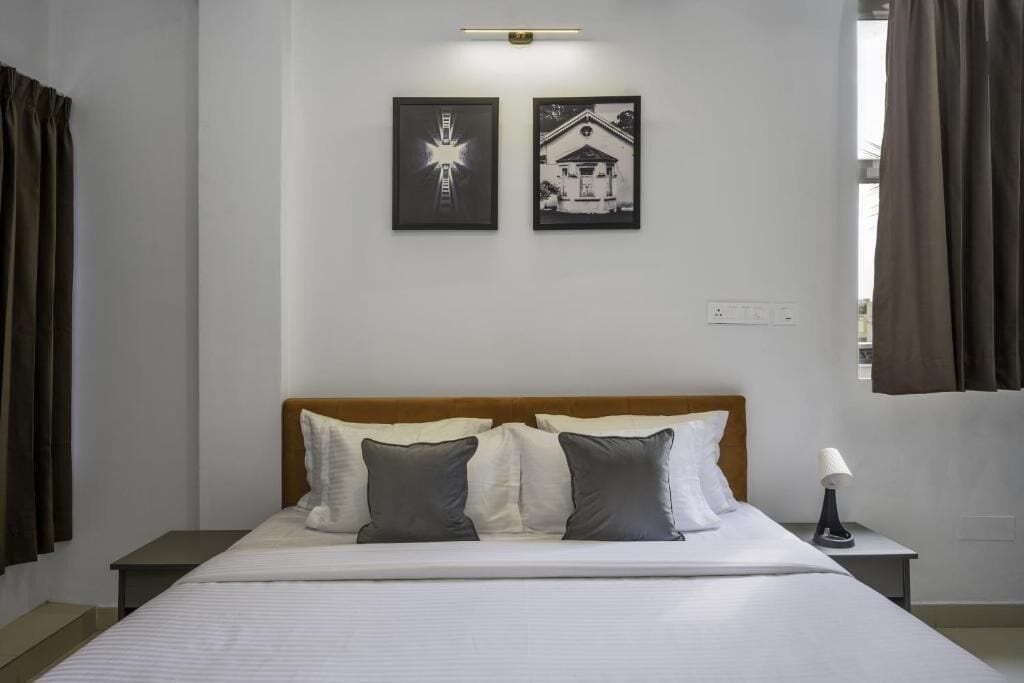 A hotel room with a bed, two pillows, a nightstand, a lamp, and two framed pictures on the wall.